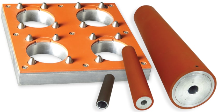 On the left is a custom nesting tray or support fixture with registration pins and a silicone rubber seal pad. On the right are three precision ground rollers. High heat tolerant (550º F) silicone rubber is bonded to the roller metal cores and the support fixture without the use of adhesives.